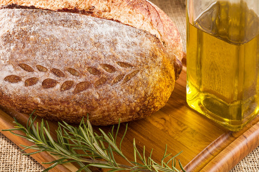 Golden extra virgin olive oil poured over crusty rustic bread on a wooden board