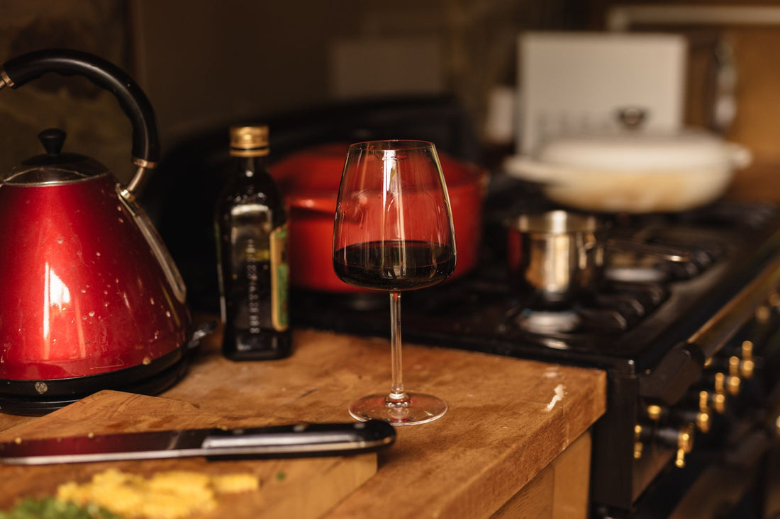 A half‑filled glass of deep red Cannonau wine on a wooden table with olives and bread, showing the wine's rich colour